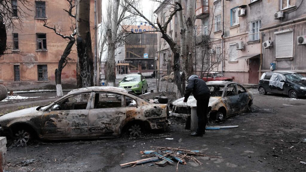 A picture in Ukraine with 2 burned cars and a man standing near the cars