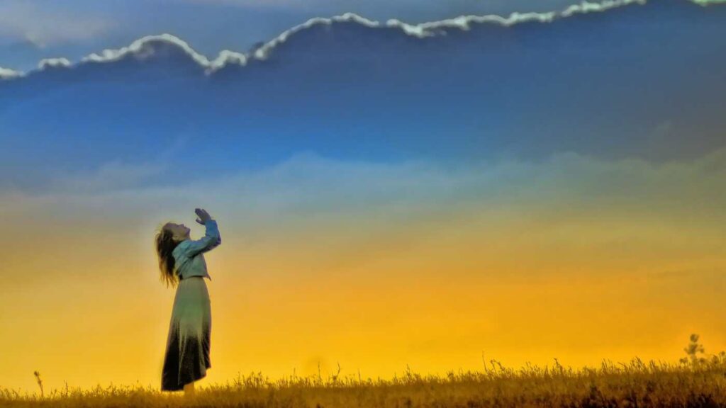 Image of a woman praying in the open field with grasses